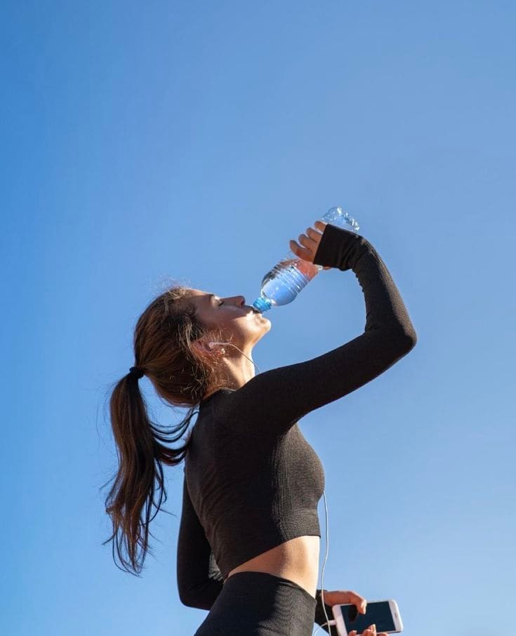 A woman taking a hydration break outdoors, phone in hand