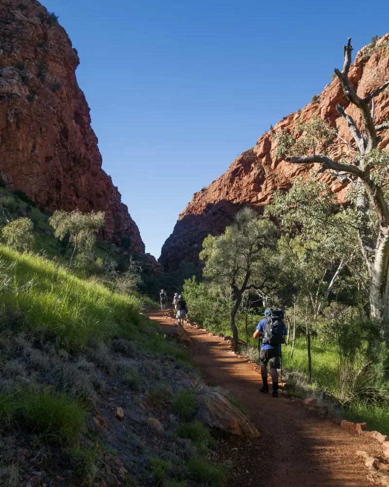 Hikers on a red dirt trail through a gorge